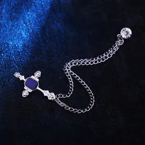 Nahaufnahme einer silbernen Kreuz Brosche mit blauem Stein, Kette und Punk Stil.
