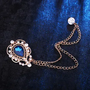 Detailaufnahme der goldenen Tropfen Brosche mit blauem Kristall und einer feinen Kette.