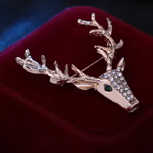 Primo piano della spilla a testa di cervo dorata con strass brillanti e occhio verde.