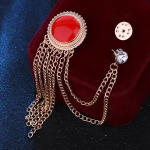 Gold-tone chain tassel brooch detail shot with red enamel round element and rhinestone pin.