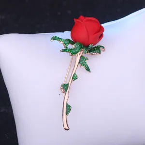 Elegante rote Rosen Broche mit gruenen Blaettern und goldener Stange fuer Damenbekleidung.