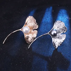 Vista detallada de broches de perlas con hoja de ginkgo, textura metálica y perlas elegantes.
