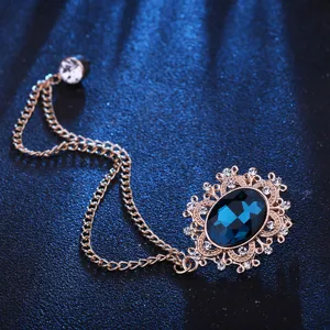 Close-up detail of vintage court style blue gemstone brooch with decorative chain and rhinestones.