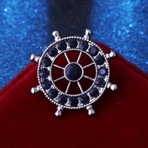 Detailed close-up of a silver nautical ship wheel brooch set with dark blue rhinestones.