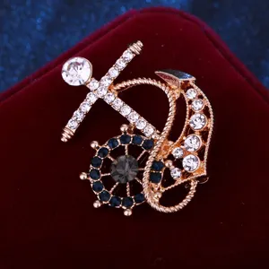 Primer plano de broche dorado de ancla y timón con cristales de estrás transparentes y azules.