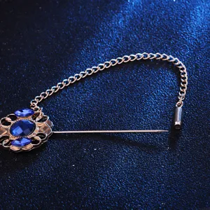 Détail de broche vintage avec strass bleus étincelants et chaîne en métal doré.