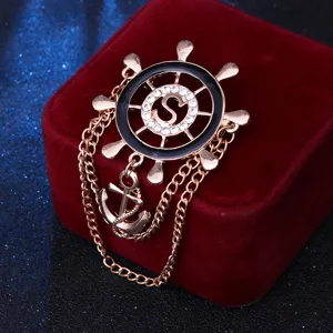 Vista detallada de broche timón de barco estilo náutico con letra S de diamantes y borla de ancla.