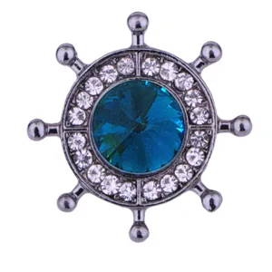 Detailed shot of a nautical ship wheel brooch with blue crystal and rhinestones.
