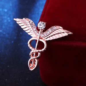 Gros plan detail de la broche strass ailes ange serpent caducee or rose accessoire chic.