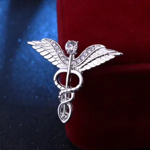 Gros plan détaillé de la broche vintage argentée ailes d'ange et caducée serpent avec strass.