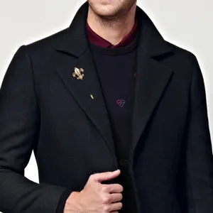 Close-up detail of a vintage gold-toned metal fleur-de-lis lapel pin on men's black suit coat.