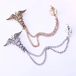 Closeup of vintage metal brooch with caduceus and anchor linked by chain, detailed design.