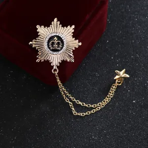 Close-up of golden crown brooch with rhinestone details and dangling star chain pendant.
