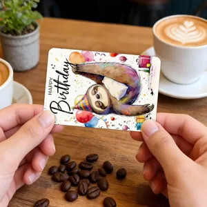 Close-up detail of a cute cartoon sloth birthday greeting card held in hands at a cafe.
