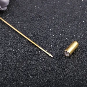 Close-up detail shot of a gold-tone long brooch pin and metal cap on sparkly dark background.