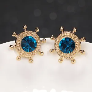 Close-up detail of gold-toned ship helm lapel pin with sparkling dark blue crystal center.