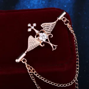 Vue détaillée d'une broche croix ailes d'ange dorée avec des strass étincelants et chaînes.