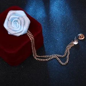 Vue détaillée de la broche fleur de rose en tissu bleu avec double chaîne dorée.