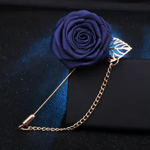Vue détaillée d'une broche rose en tissu bleu marine avec chaîne dorée sur support.