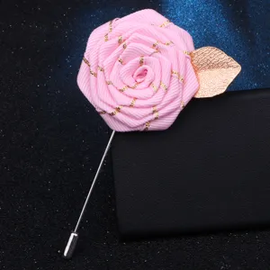 Close-up detail of handmade pink ribbon rose brooch with gold leaf and metal pin accessory.