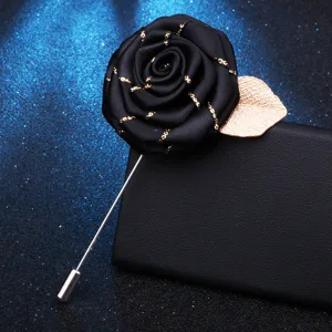 Gros plan d'une broche rose en tissu noir avec feuille d'or et longue épingle métallique.