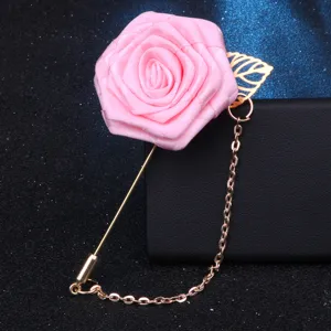 Gros plan détaillé d'une broche boutonnière rose en tissu avec longue épingle dorée et chaîne.