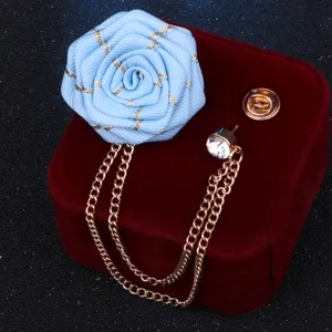 Nahaufnahme einer blauen Bandrosen-Brosche mit Goldketten und Strass-Reversnadel.