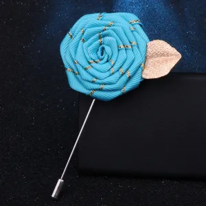 Close-up of handmade blue ribbon rose brooch with gold leaf detail, elegant lapel pin accessory.