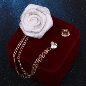 Gros plan d'une broche rose en tissu blanc avec chaînes à pampilles dorées et strass.