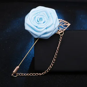 Broche rose en tissu bleu avec chaîne dorée, détail de feuille et longue épingle costume.
