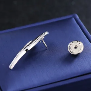 Silver feather lapel pin detail shot, elegant metal brooch on blue display box surface.