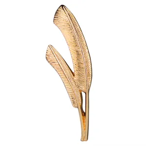 Gold double leaf brooch detail, showing the fine feather carving and glossy metallic surface.