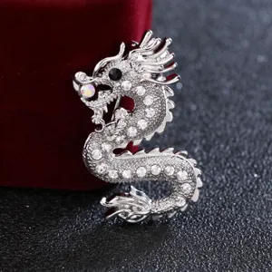 Vista ravvicinata e dettagliata della spilla a forma di drago argento con strass luminosi.