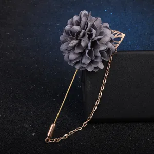 Gros plan détaillé d'une broche florale en tissu gris avec longue chaîne dorée et feuille.