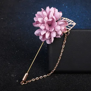 Gros plan d'une broche fleur en tissu rose avec feuille d'or, longue épingle et chaîne élégante.