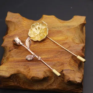 Close-up detail of metal lapel pins featuring golden flower and rose designs on wooden prop.