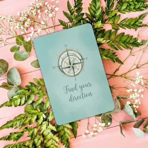Nahaufnahme einer Motivationskarte mit Kompass-Design auf pinkem Blumenhintergrund.