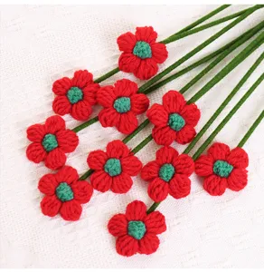 Detailed macro view of handmade red crochet flowers with long green stems on white fabric