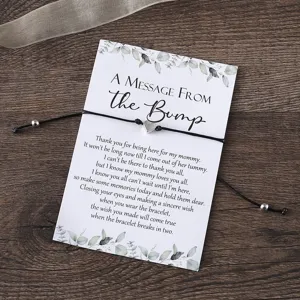Detailed close-up view of a black braided cord bracelet with a silver heart charm on card.