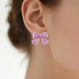 Nahaufnahme glänzender rosa Acryl-Schleife-Ohrringe am Ohr, schönes irisierendes Detail.