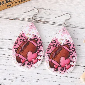 Gedetailleerde close-up van druppelvormige lederen oorbellen met football en roze hartjes.