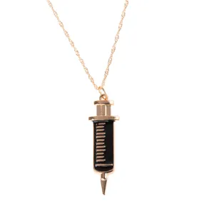 Gold tone syringe pendant necklace close up, featuring black enamel detail on fine chain link.