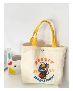 Corduroy tote bag detail showing cute rabbit embroidery, yellow handles, and sturdy texture.
