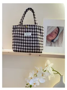 Detailed view of a chic houndstooth tweed handbag, featuring elegant pattern and soft fabric texture.