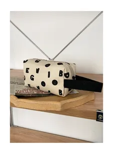 Détail de la trousse en toile avec imprimé de lettres noires et lanière latérale.