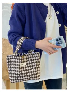 Detail shot of a stylish woolen houndstooth handbag, showcasing the portable design and texture.
