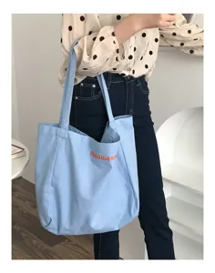 Detail view of a light blue canvas tote bag with orange letter embroidery, casual daily style.