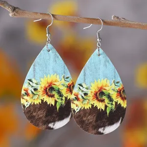 Nahaufnahme von tropfenförmigen PU Leder Ohrringen mit Sonnenblumen und Kuhmuster.