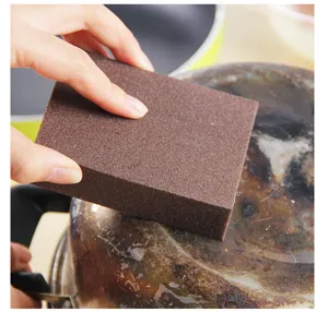 Close-up of brown emery cleaning sponge removing rust on pot bottom, efficient kitchen tool.