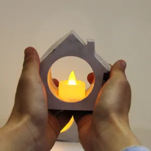 Close-up view of a minimalist house-shaped candle holder with glowing LED tealight inside.